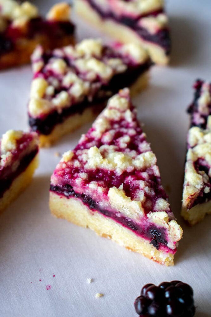 Blackberry bars with a purple filling and golden streusel topping are arranged on a white surface