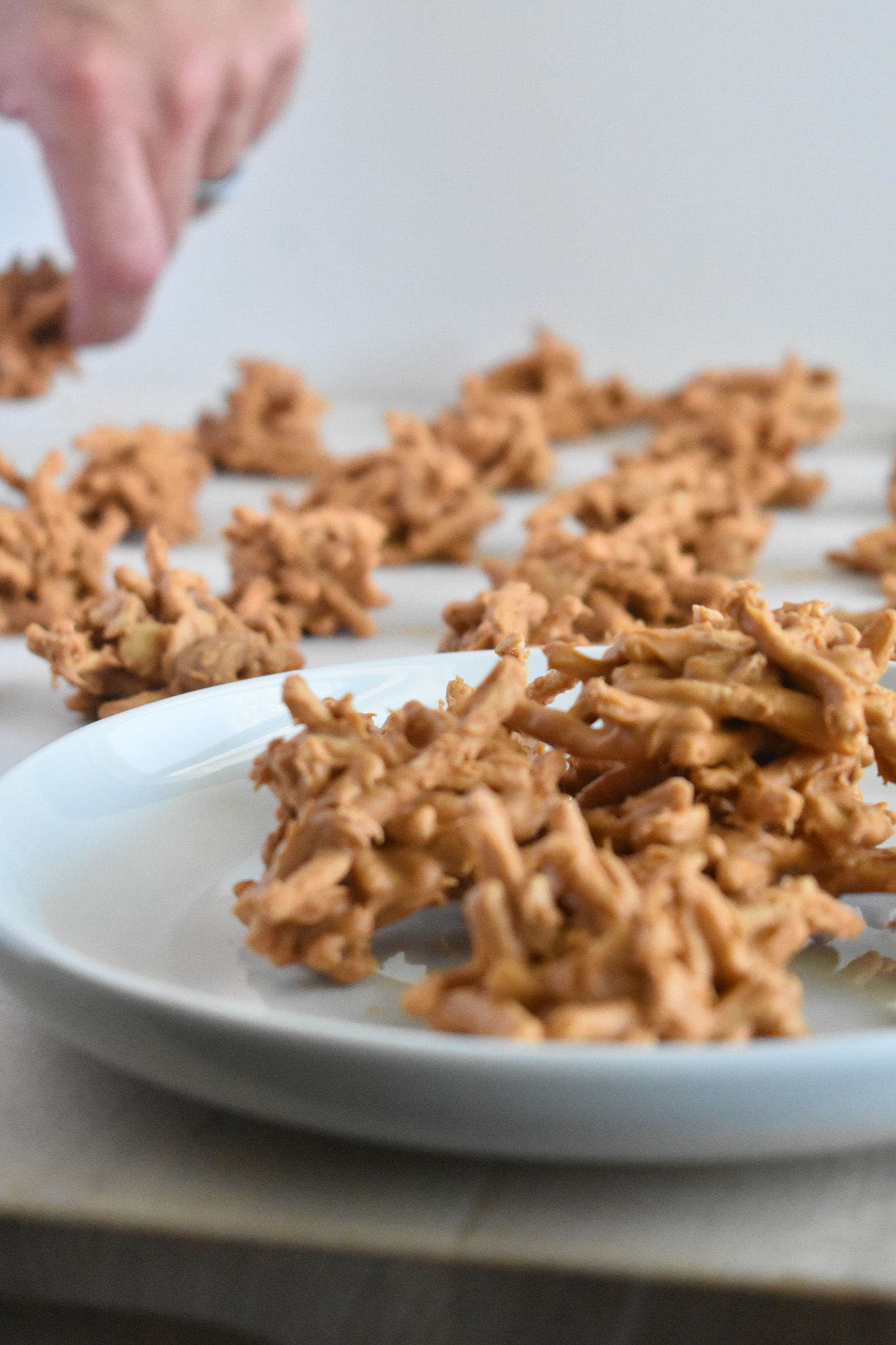 A hand picks up a no bake butterscotch haystack among many others in the foreground.