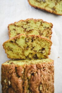 Sliced loaf of pistachio bread with a crumbly, nutty texture on parchment paper. The vibrant green interior contrasts with the golden crust.