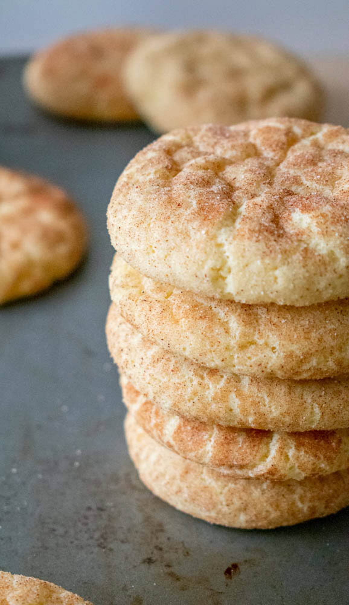 A stack of five golden brown snickerdoodle cookies dusted with cinnamon sugar on a baking tray