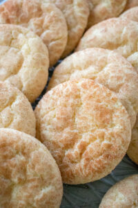 Close up of a plate of freshly baked snickerdoodle cookies. Shows light golden brown cookies with a crinkled surface and dusted with cinnamon sugar.