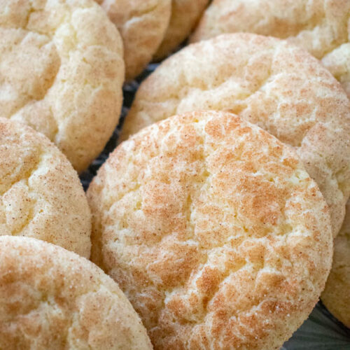 Close up of a plate of freshly baked snickerdoodle cookies. Shows light golden brown cookies with a crinkled surface and dusted with cinnamon sugar.