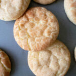 Golden brown snickerdoodle cookies with crinkled tops are arranged on a gray baking sheet