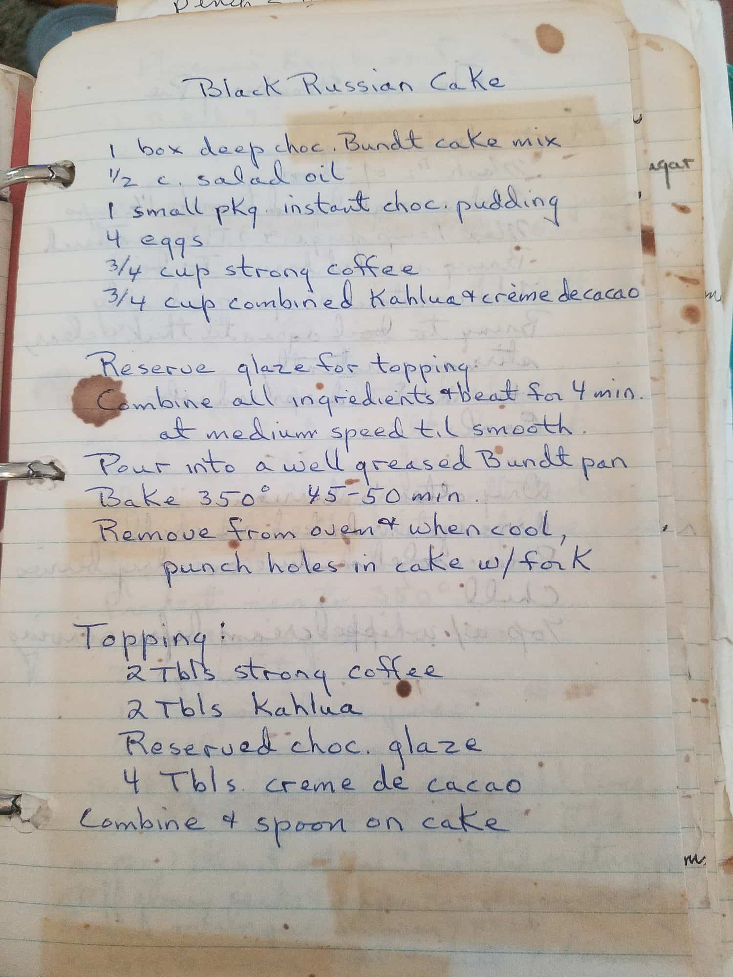 Handwritten recipe titled "Black Russian Cake" on lined paper in blue ink. Includes ingredients like coffee and Kahlua, with stains on the pages