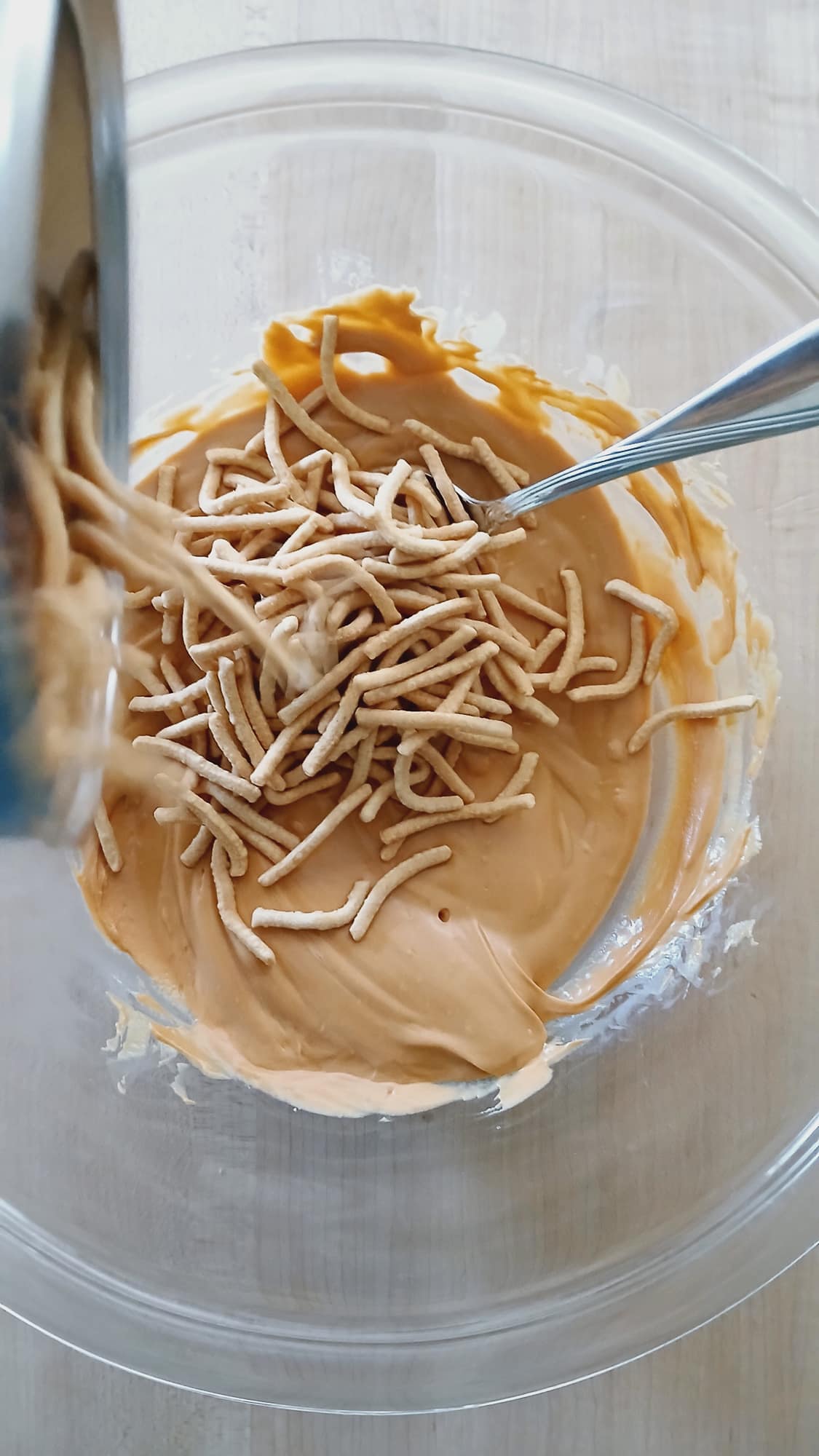 Crunchy chow mein noodles being poured into a bowl with melted butterscotch chips while making butterscotch haystacks