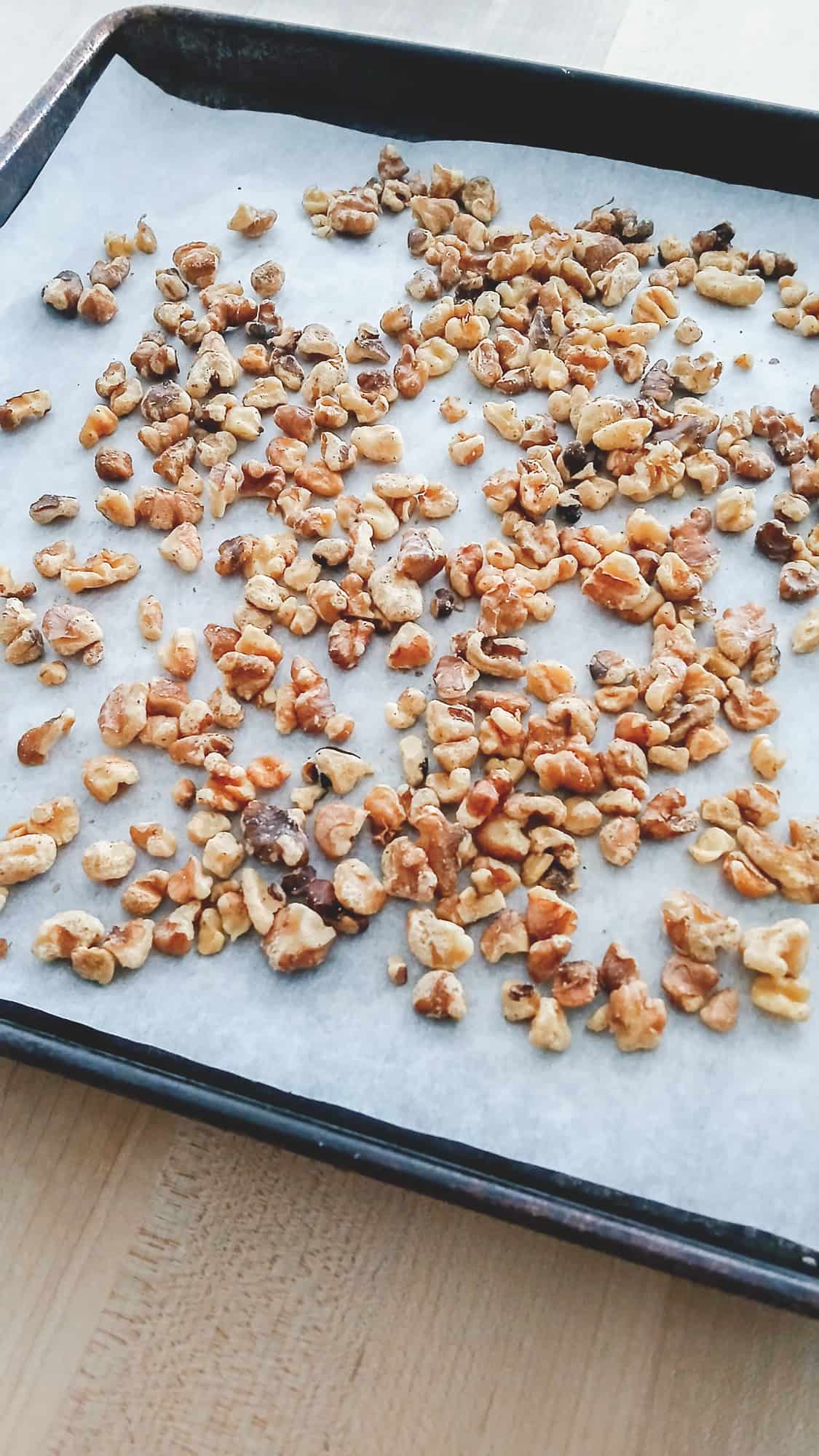 Toasted walnuts scattered on a parchment lined baking sheet. The nuts are going into the carrot cake batter.