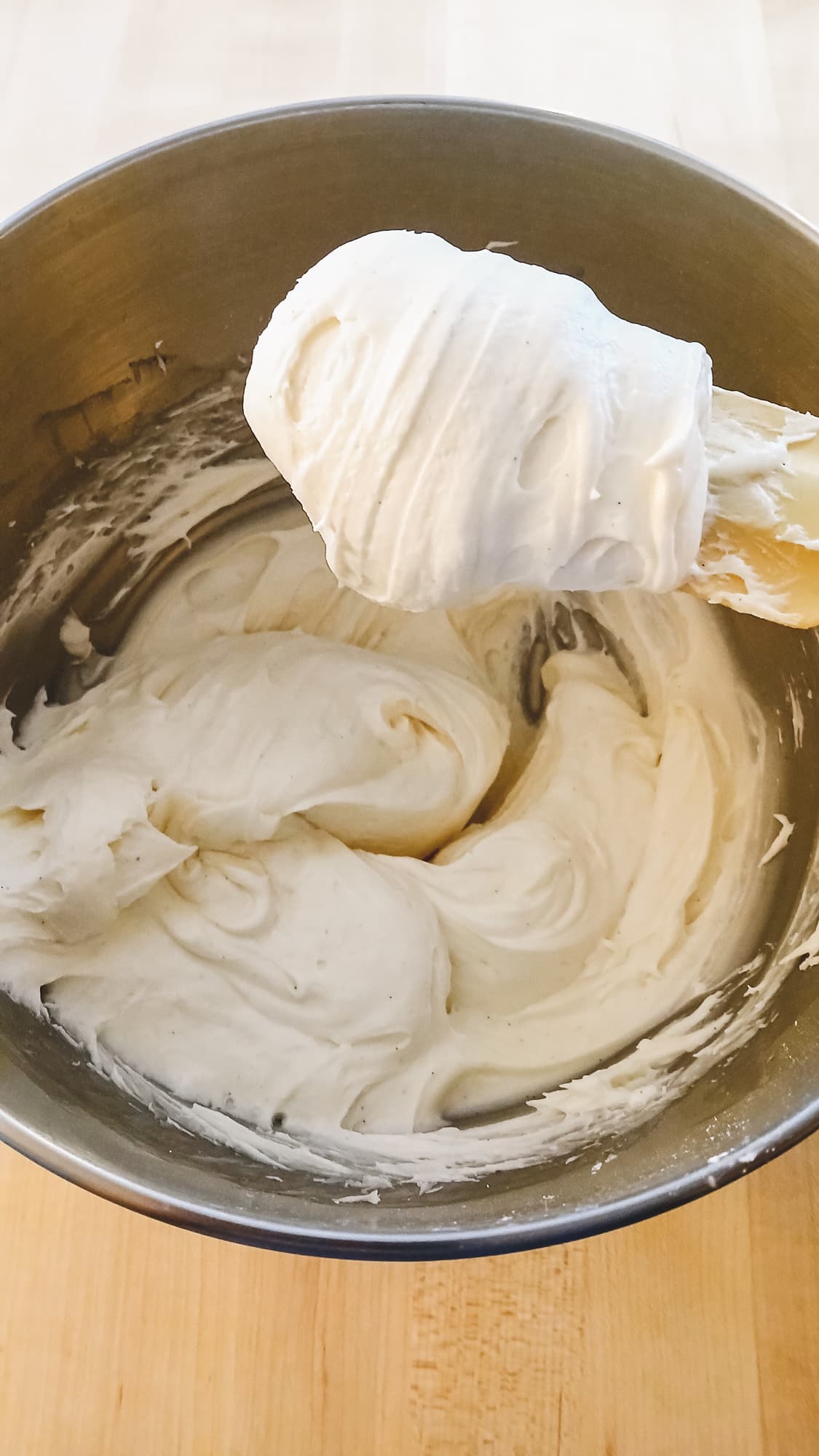 A bowl of white cream cheese frosting with a spatula. The thick, smooth texture suggests it's freshly whipped
