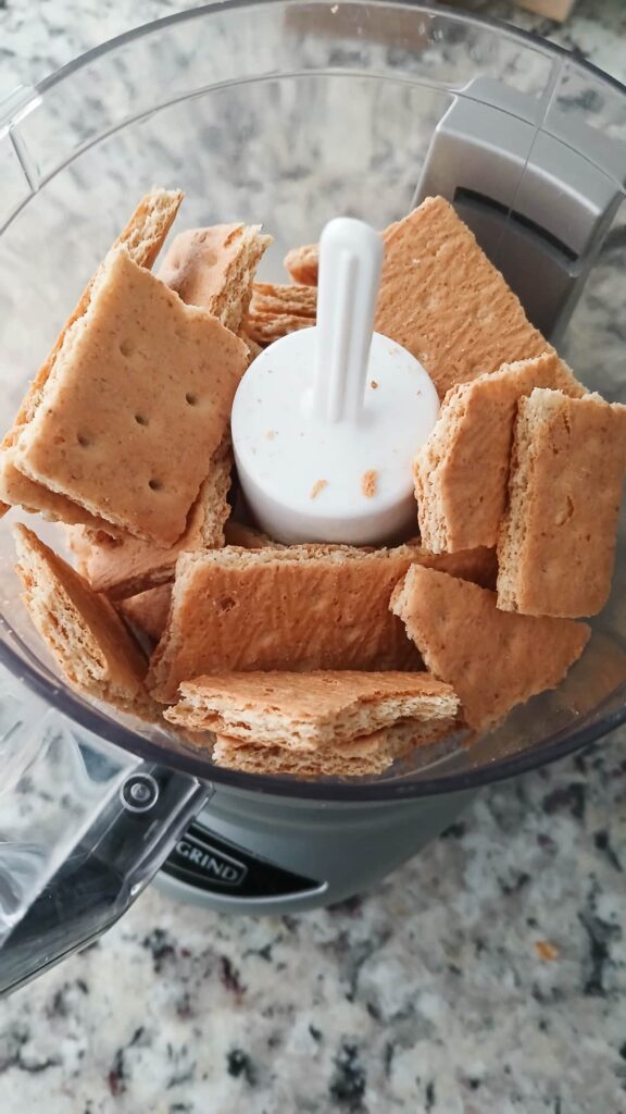 Broken graham cracker pieces inside a food processor ready to be crushed.