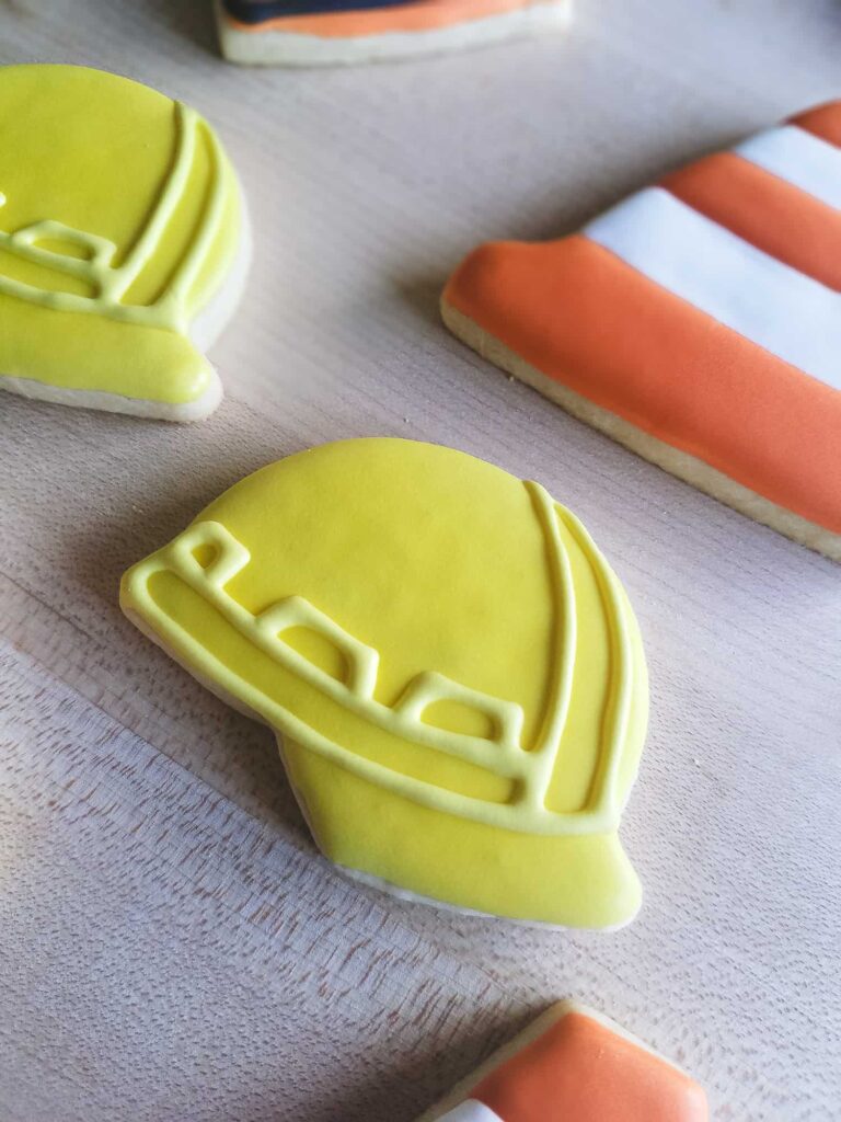 Soft cut-out sugar cookies decorated with royal icing to look like yellow construction hats and orange traffic cones.