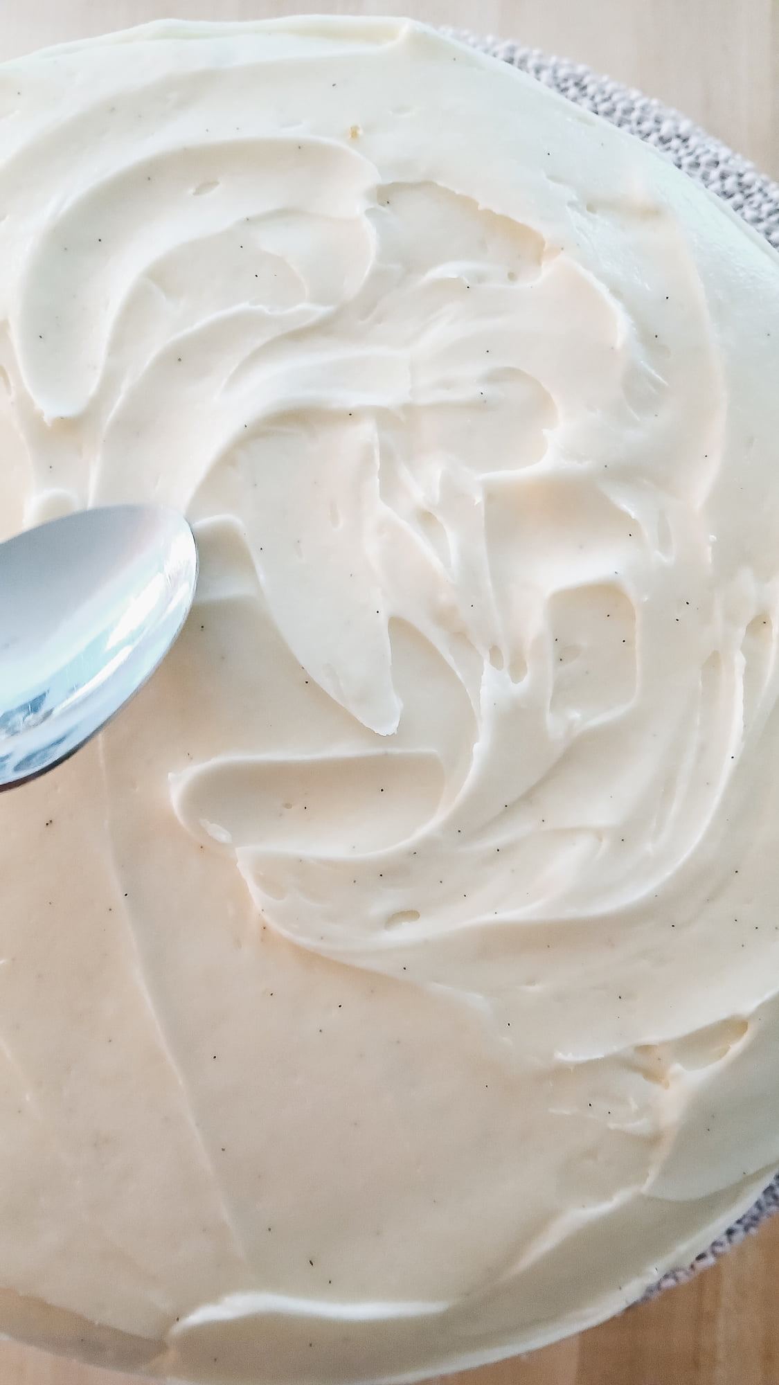 Using the back of a spoon to create rustic frosting swirls with visible vanilla bean specks.