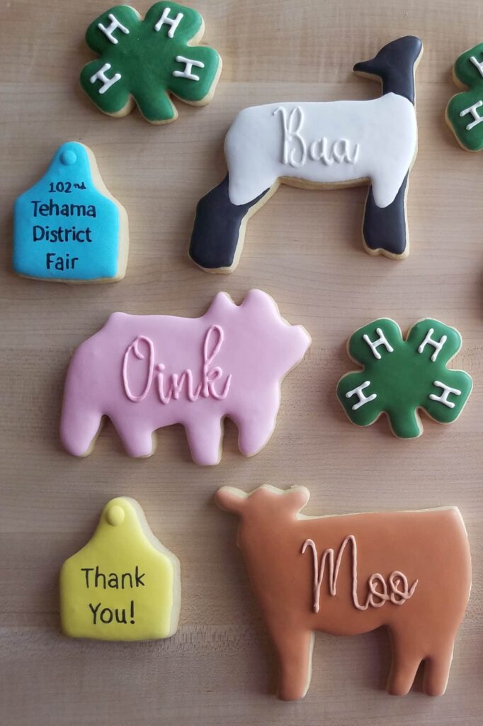 Assorted farm-themed cookies decorated with royal icing, including animal shapes with "Oink," "Baa," "Moo," green 4-H clovers, and fair-themed tags.
