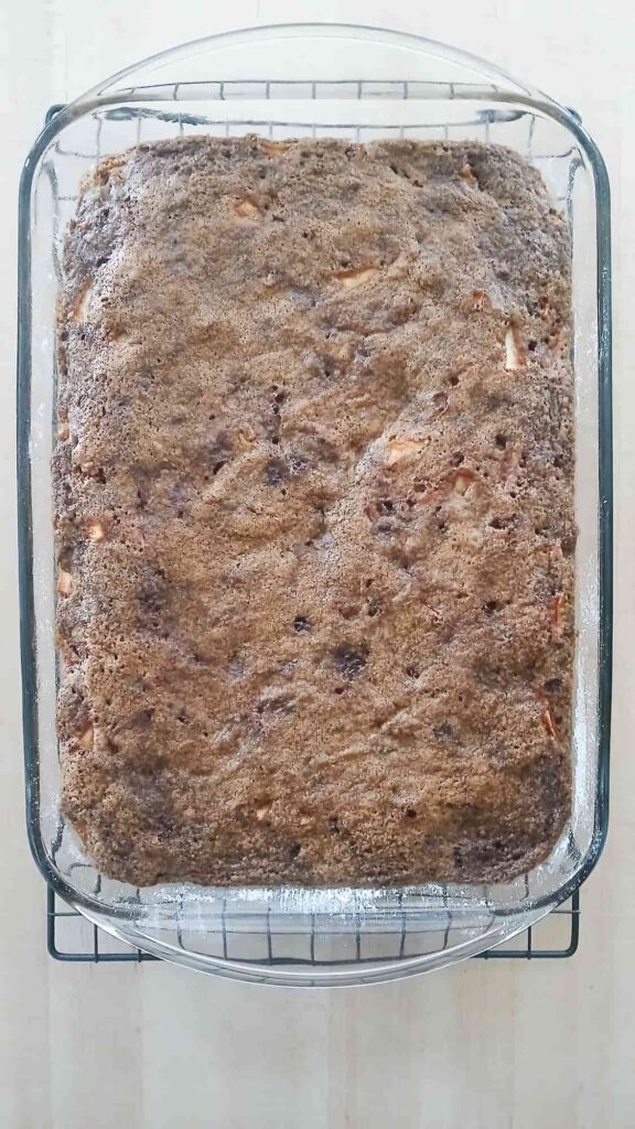 Apple cake in a glass baking dish after it has been baked and now it is cooling on a cooling rack.