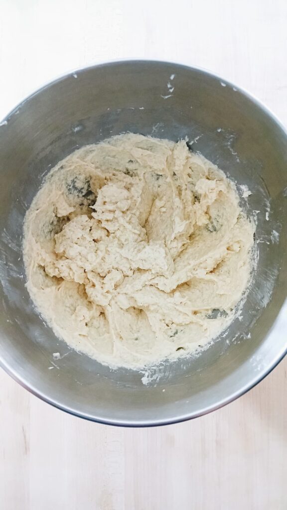 A top-down view inside a silver metal stand mixer bowl, showing the butter and sugar creamed together into a pale, smooth, and fluffy mixture.