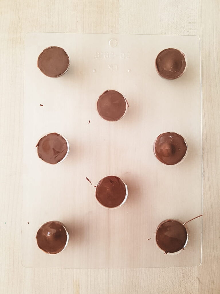 Plastic candy mold shows the entire mold layered and filled with chocolate on the top which will become the bottom of the candy