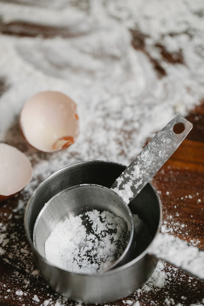 Close-up of flour, eggshells, and baking utensils on a wooden surface, perfect for food blogs.