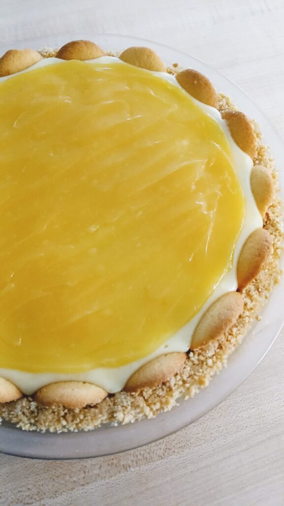 A layer of lemon curd has been spread over the top of a chilled lemon icebox pie. The lemon curd gives the pie a pop of bright yellow color