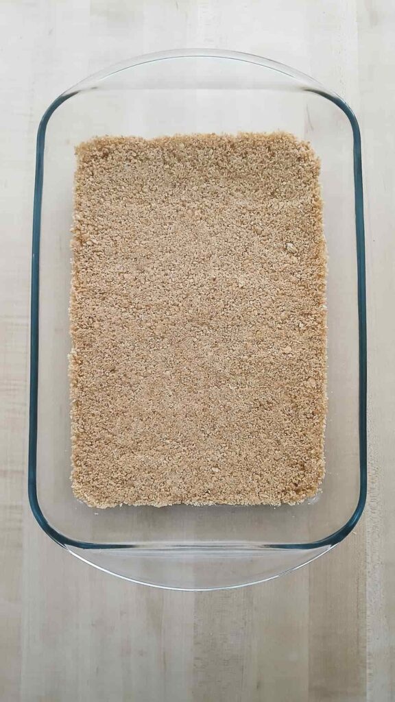 A glass baking dish filled with an even layer of finely crushed, light brown graham cracker crumbs in the bottom
