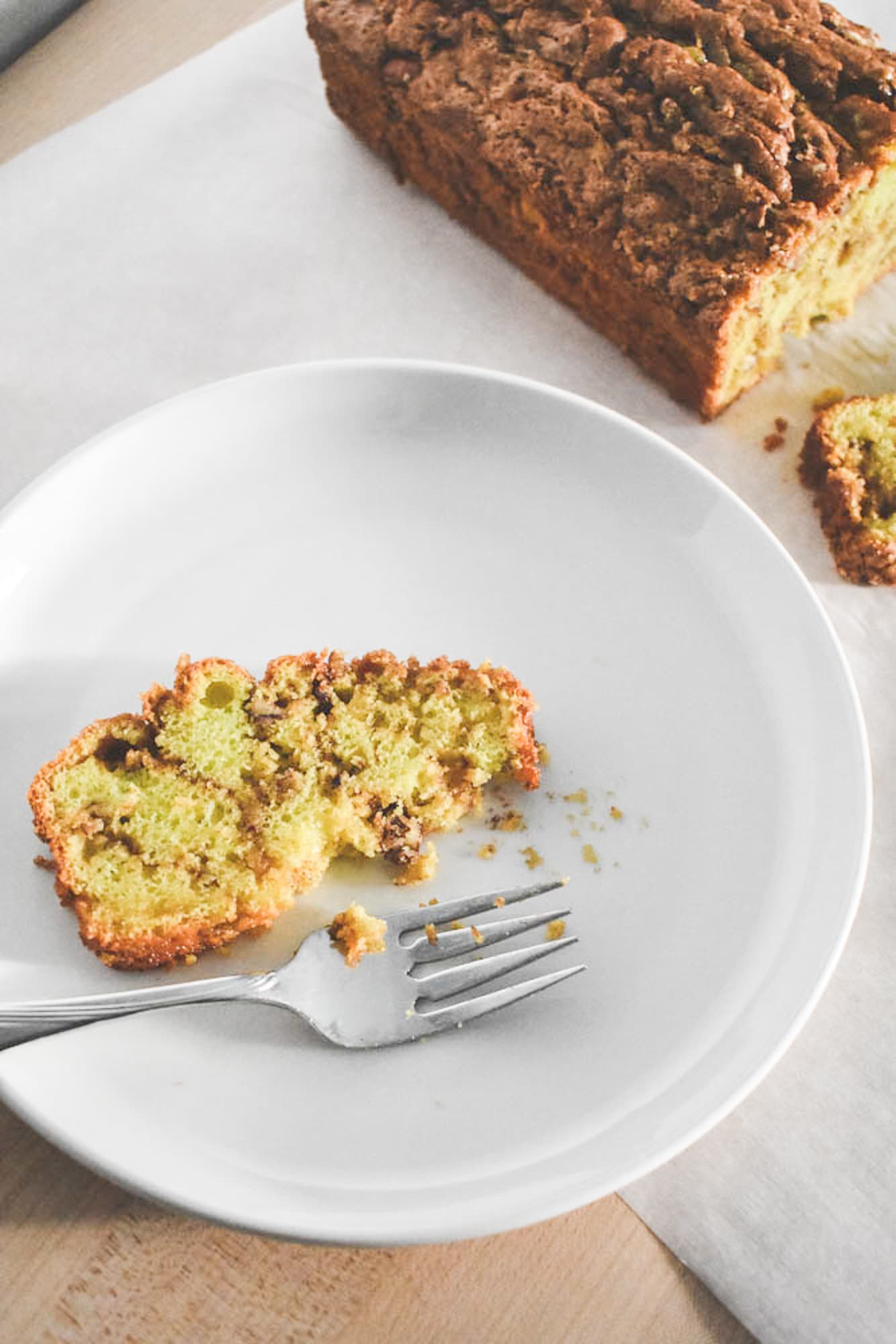 Sliced of pistachio bread on a plate with a fork. The bread loaf is in the background