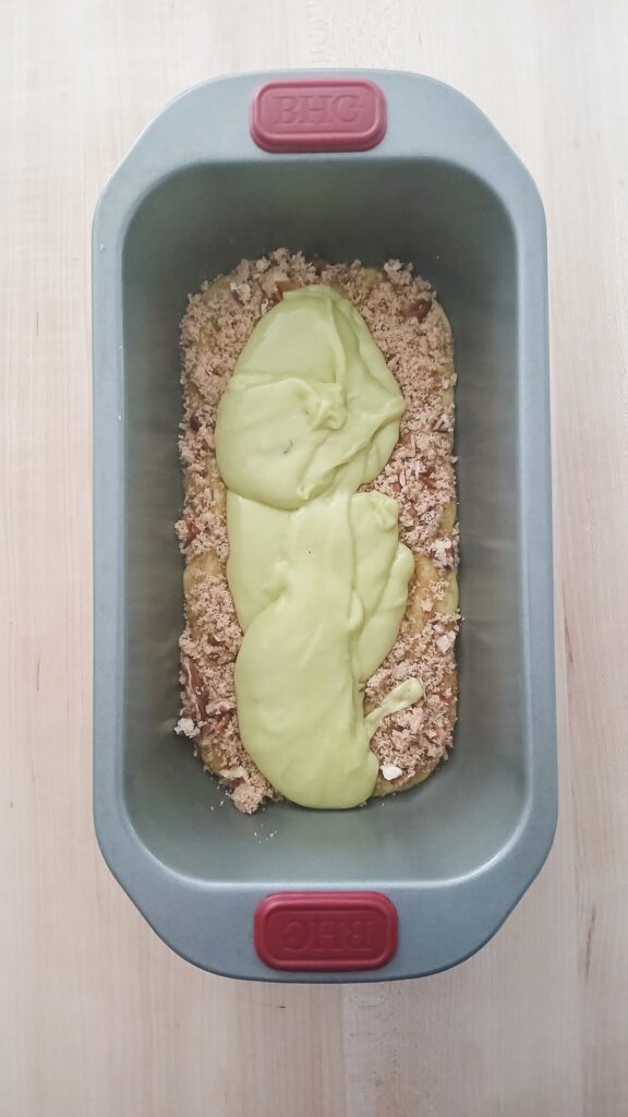 An overhead shot showing the first layer of dark brown sugar, cinnamon, and chopped pecan crumble sprinkled generously over the green batter, followed by a second layer of batter being spread on top.