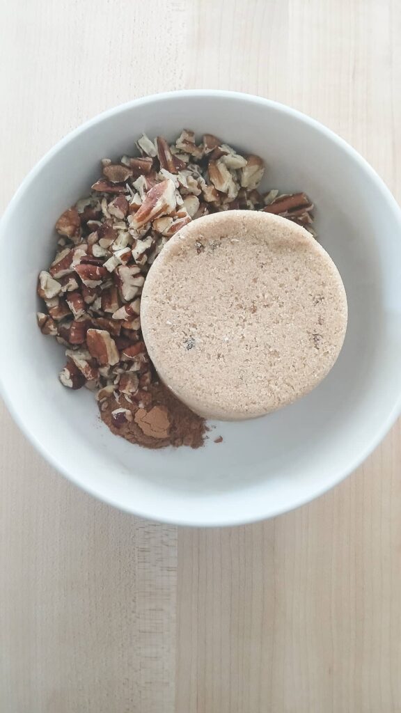 A white bowl contains chopped pecans, a mound of brown sugar, and a bit of cinnamon to make cinnamon swirl.