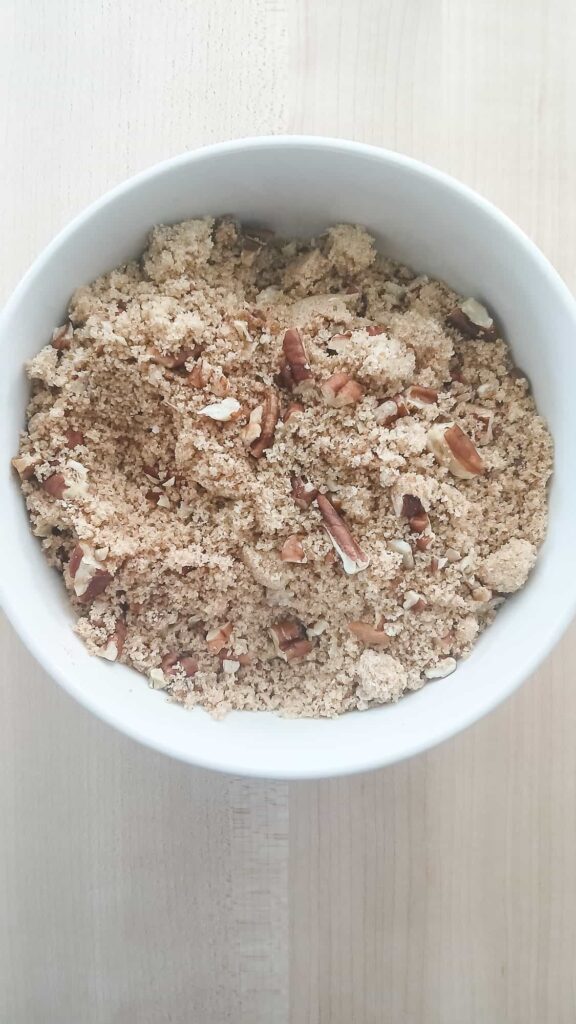 A white bowl filled with crumbly streusel mix, featuring brown sugar and chopped pecans. This swirl will be layered into pistachio bread.