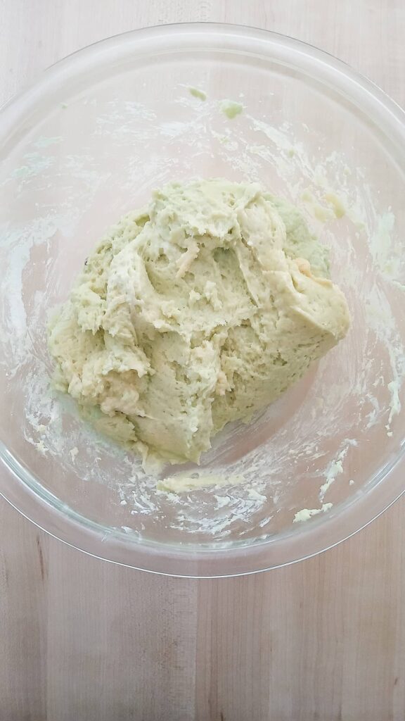 A mixing bowl filled with an incredibly thick, green batter made of cake mix, pistachio pudding, and sour cream before the eggs are added.