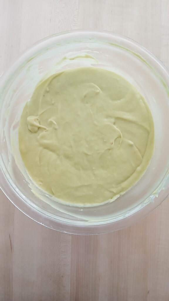 The finished pistachio bread batter in a mixing bowl showing a smooth, glossy texture and a signature pale green color after all four eggs have been fully incorporated.