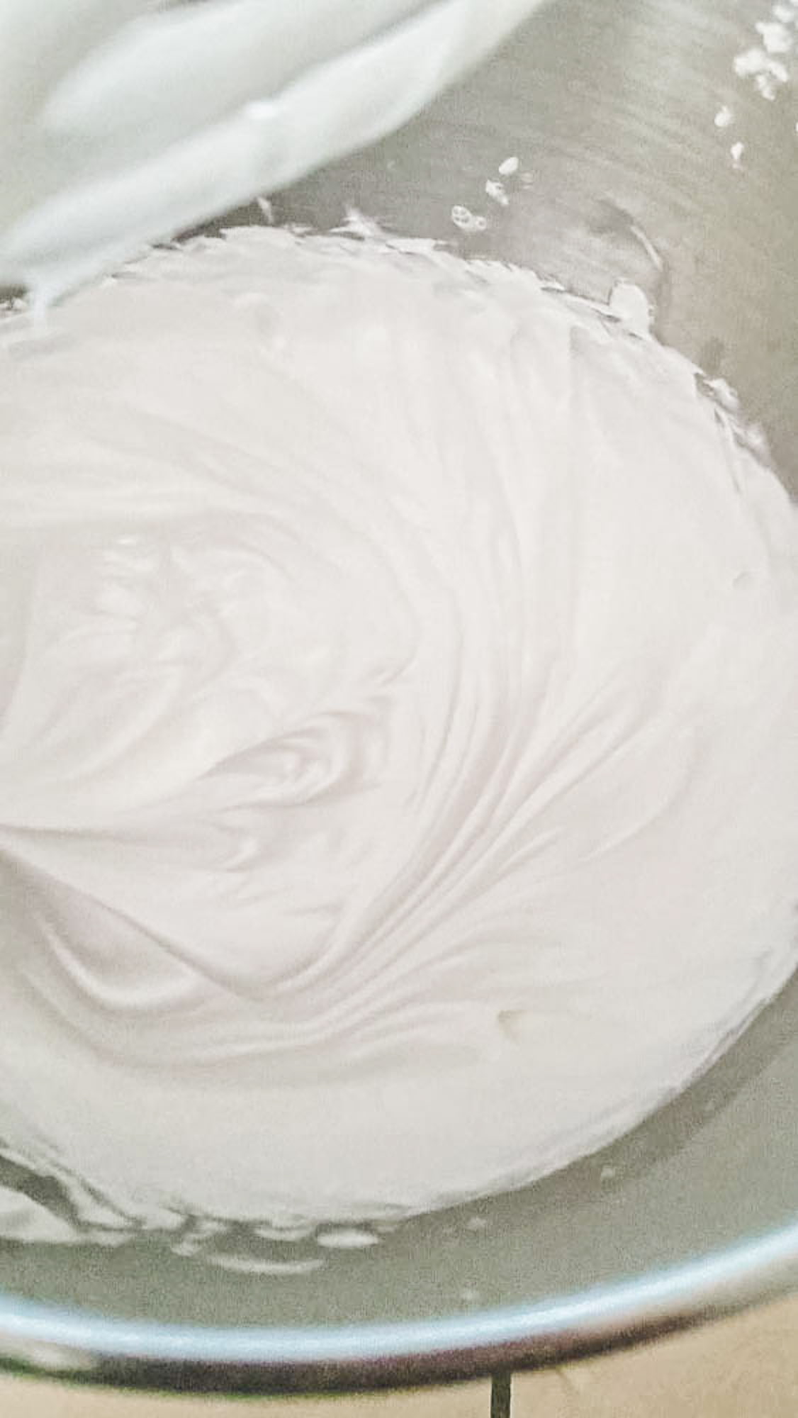 Bowl of fluffy white royal icing being mixed to peaks, showing smooth and glossy texture.