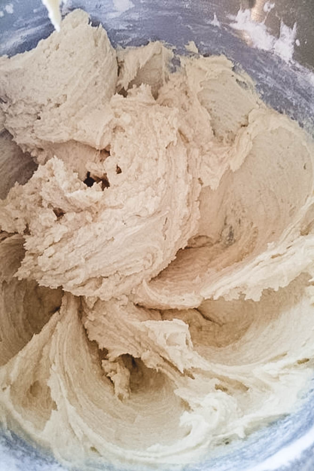 A close-up of thick Snickerdoodle cookie dough made with stick margarine and cream of tartar in a silver stand mixer bowl