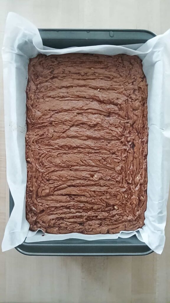 A 9x13 pan of chocolate peanut brittle fudge spread into an even layer and ready to cool at room temperature until firm