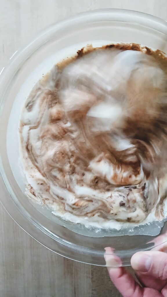 Stirring the chocolate and marshmallow mixture vigorously in a glass bowl to create a smooth and glossy chocolate fudge base.