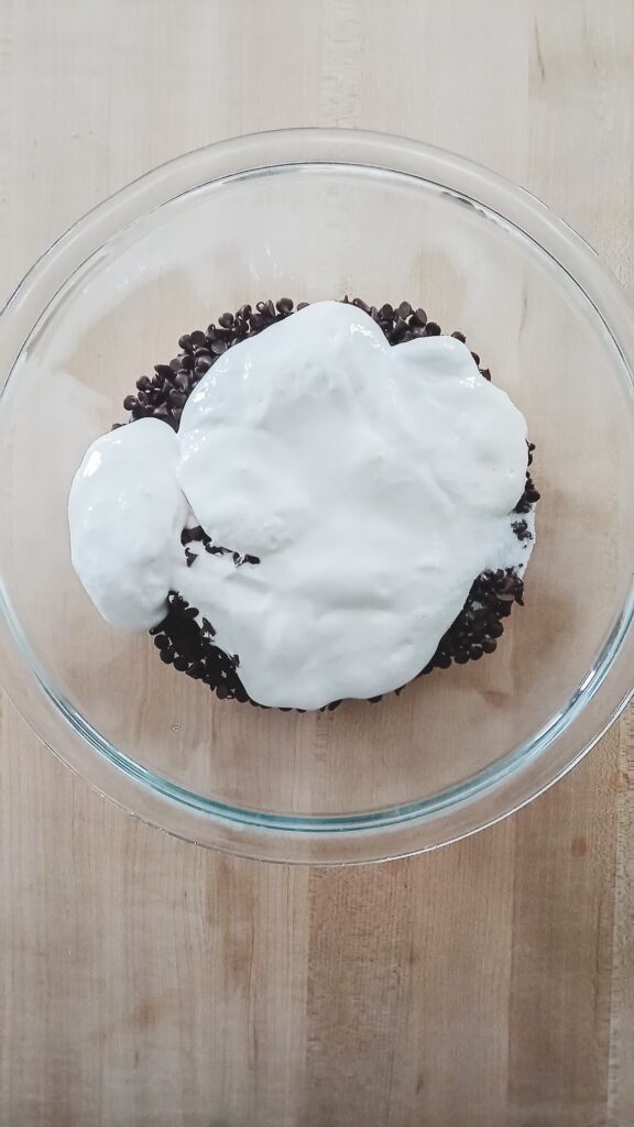 A glass mixing bowl filled with semi-sweet chocolate chips and marshmallow fluff prepared for the pour-over fudge method to ensure a smooth, creamy texture.