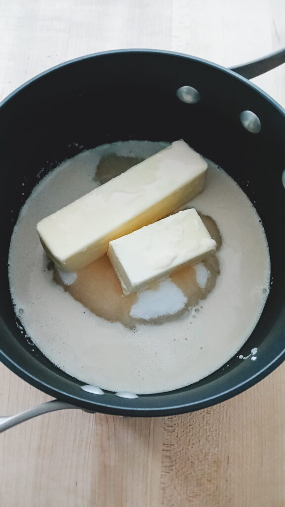A heavy-bottomed saucepan on the stove filled with evaporated milk, butter, and granulated sugar ready to be melted into a smooth fudge base.