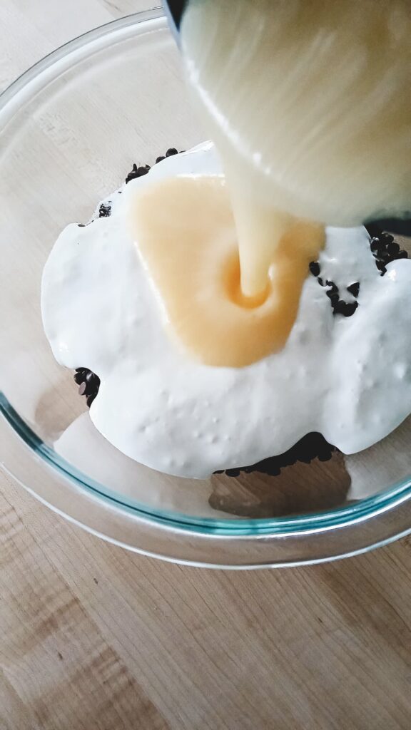 Pouring the hot boiling sugar mixture over a bowl of marshmallow fluff and chocolate chips using the pour-over method for smooth fudge.