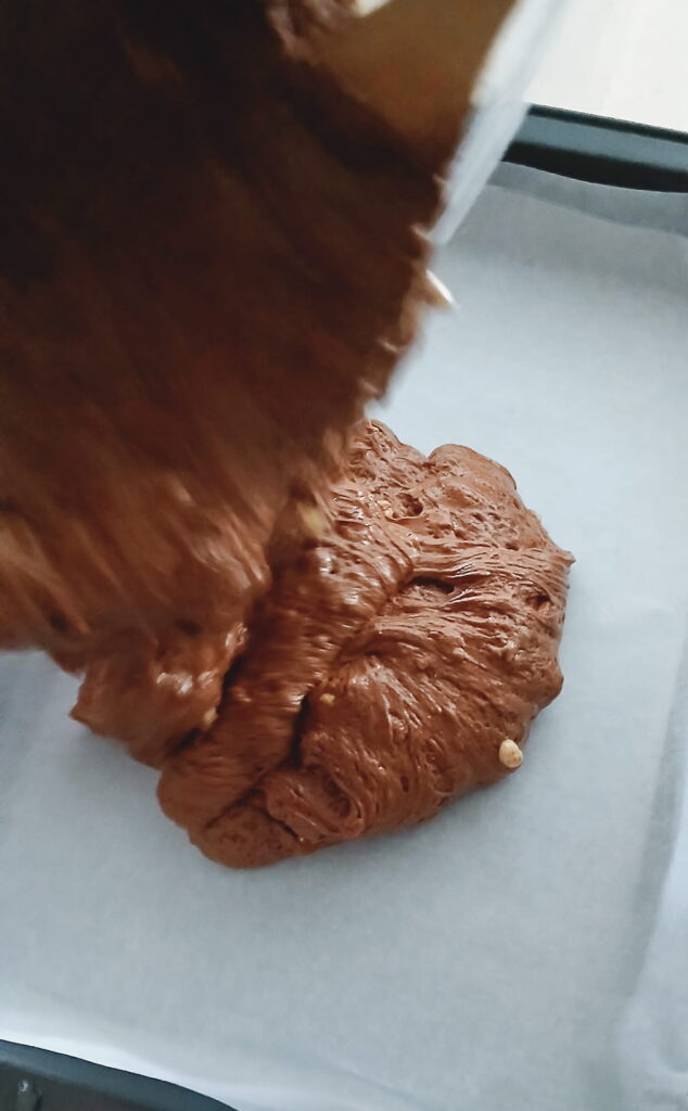 Pouring the thick peanut brittle fudge mixture into a 9x13 pan lined with parchment paper before spreading it into an even layer.