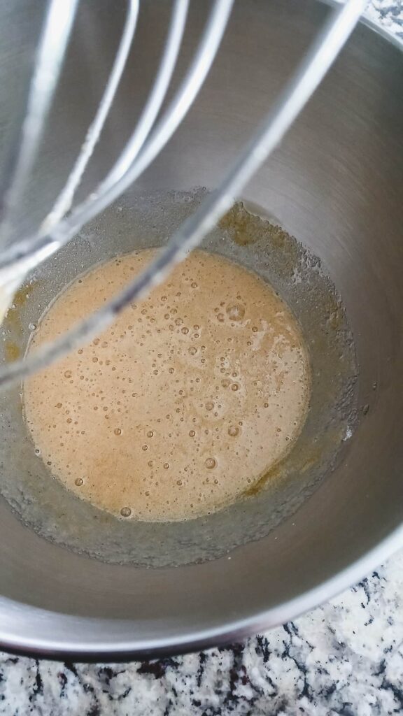 The early stages of the egg and sugar mixture in a stand mixer bowl, showing a light tan and slightly frothy texture.