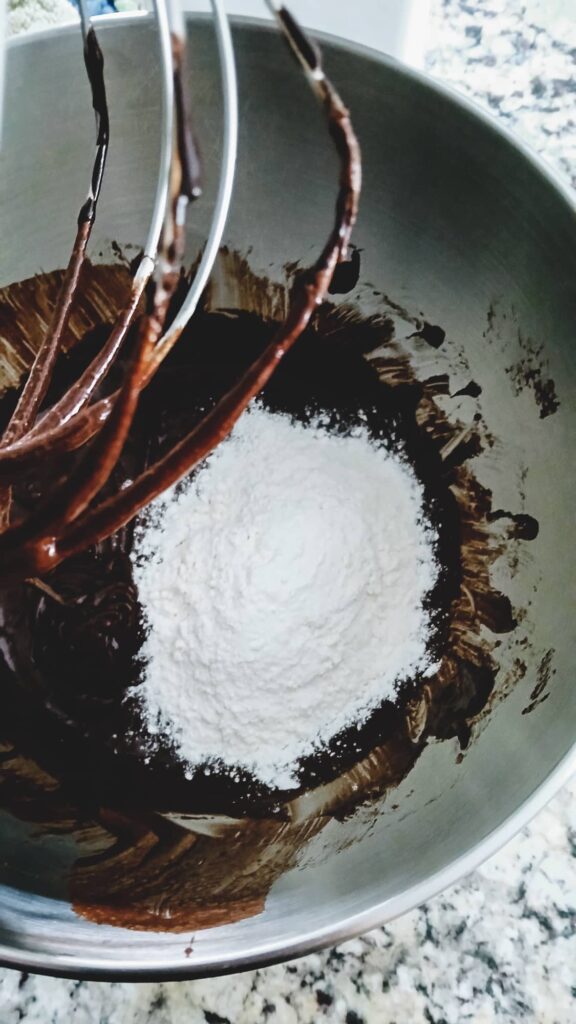 The chocolate batter in a stand mixer bowl with a portion of white all-purpose flour on top, ready to be gently mixed in until just combined.
