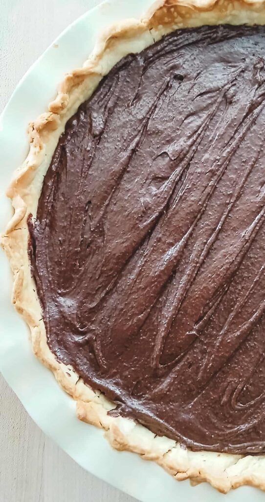 A close-up of the thick, dark chocolate brownie batter smoothed evenly into the golden, blind-baked pie crust and ready for the oven.