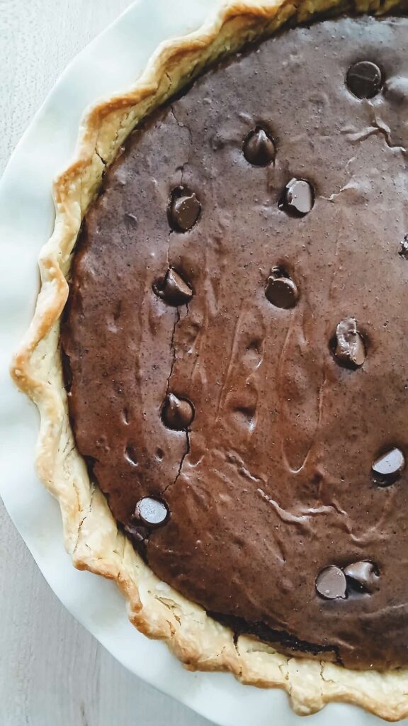 A close-up of the finished brownie pie showing the signature shiny, crackly top and the slightly puffed edges of the buttery crust.