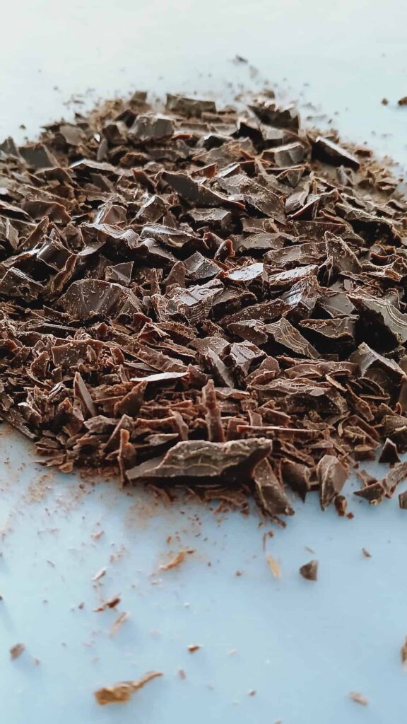 A close-up shot of a bittersweet chocolate bar finely chopped into uniform pieces on a blue cutting board.