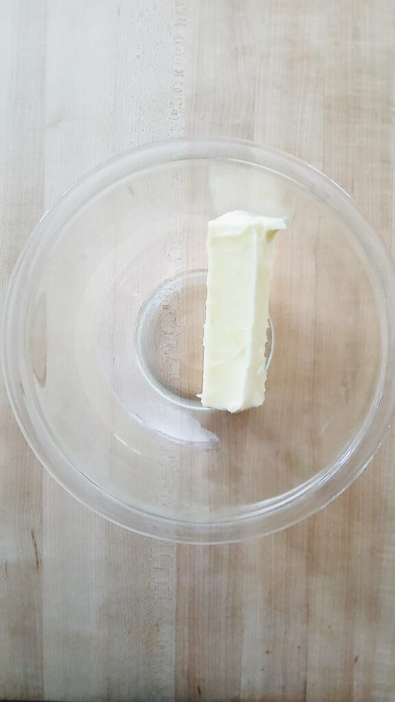 A whole stick of butter in a clear, microwave-safe glass bowl ready to be melted for the pie filling.