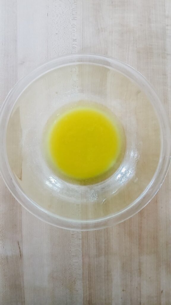 Melted, golden yellow butter in a clear glass bowl immediately after being heated in the microwave.