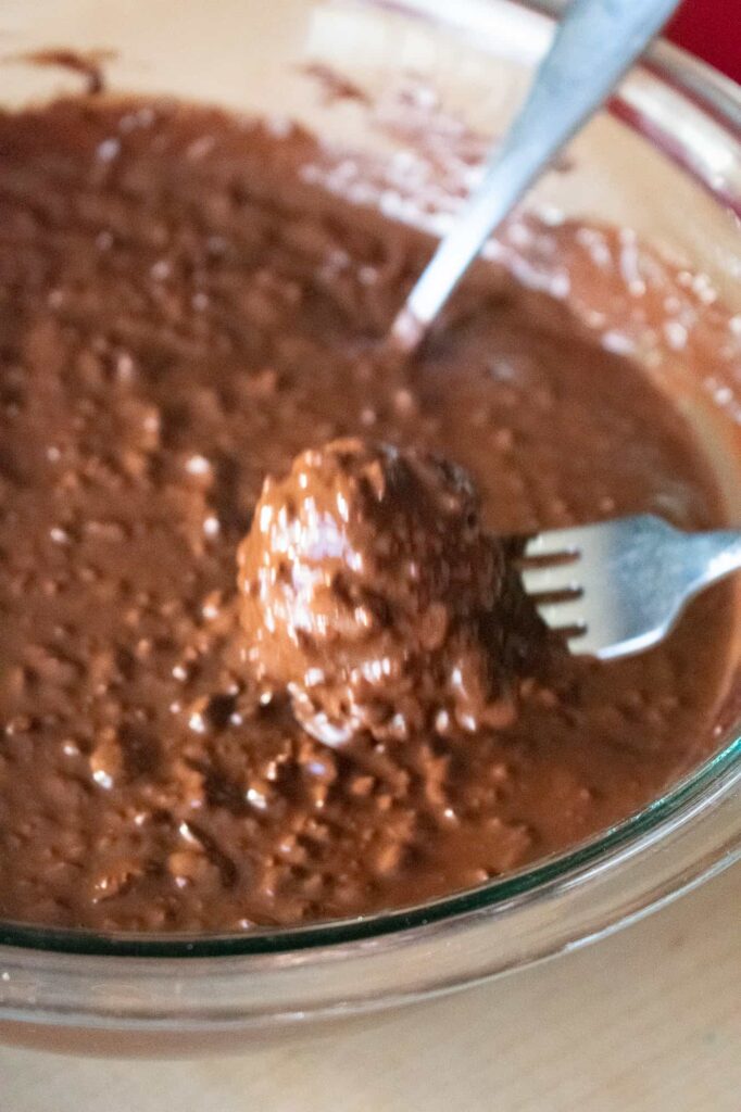 A fork shakes off excess chocolate while dipping cherry mash candy center into chocolate coating