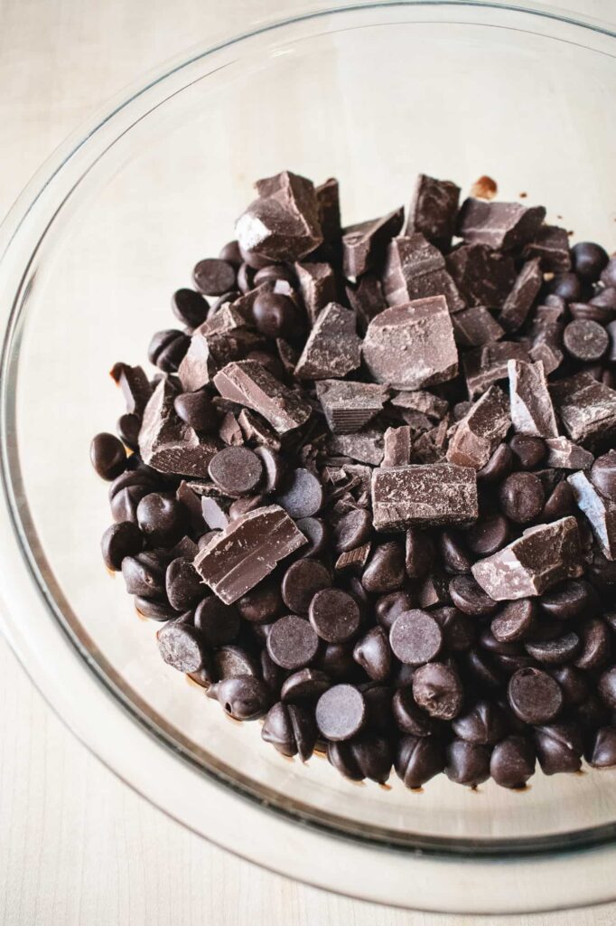 A glass bowl filled with dark chocolate chips and chunks on a light wooden surface
