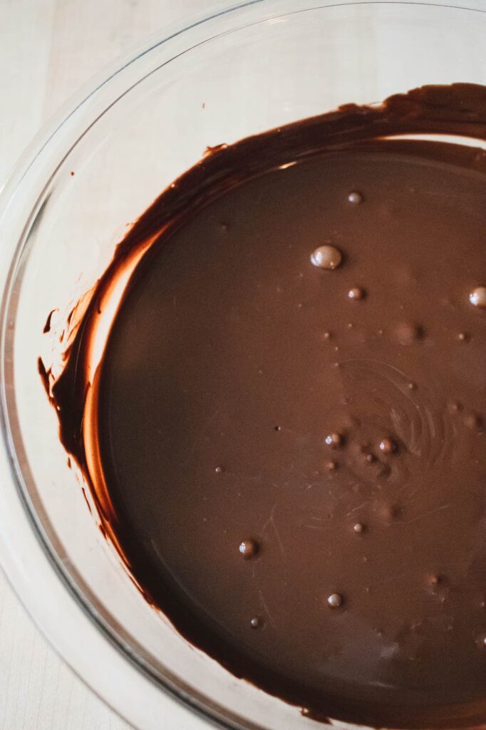 A glass bowl filled with smooth, melted dark chocolate, with a few bubbles on the surface