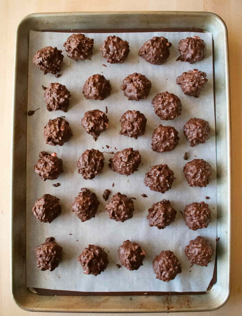 Rows of chocolate-covered homemade candy with textured surfaces are neatly arranged on a parchment-lined baking sheet