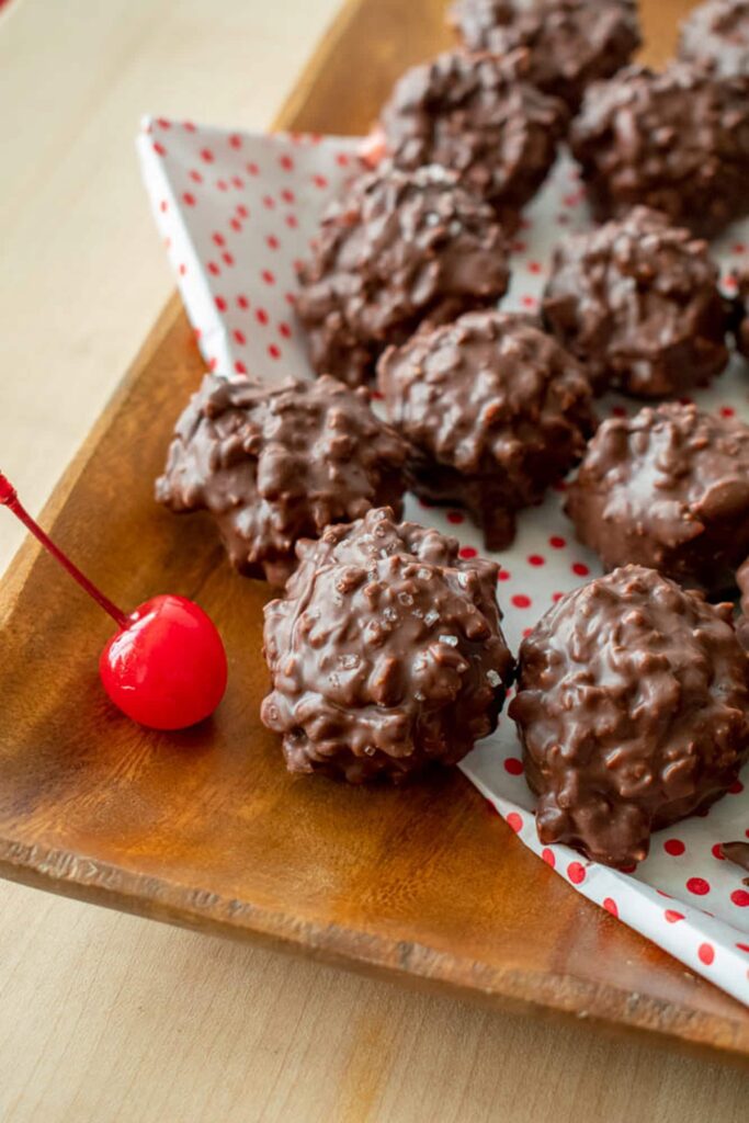 Cherry mash candy arranged on a wooden tray lined with polka dot paper, accompanied by a single bright red cherry