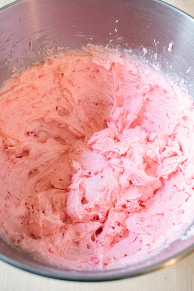 A metal mixing bowl filled with fluffy pink cherry mash filling. Speckled with small red cherry bits can be seen throughout