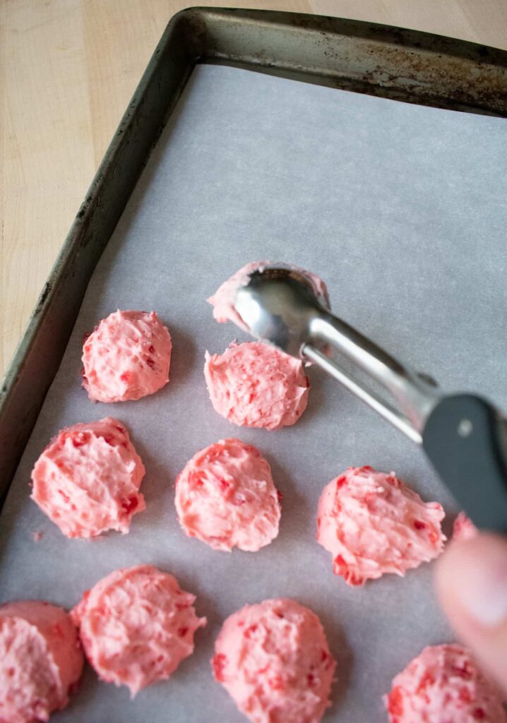 Scoops of pink cherry mash filling scooped onto a parchment-lined baking sheet.