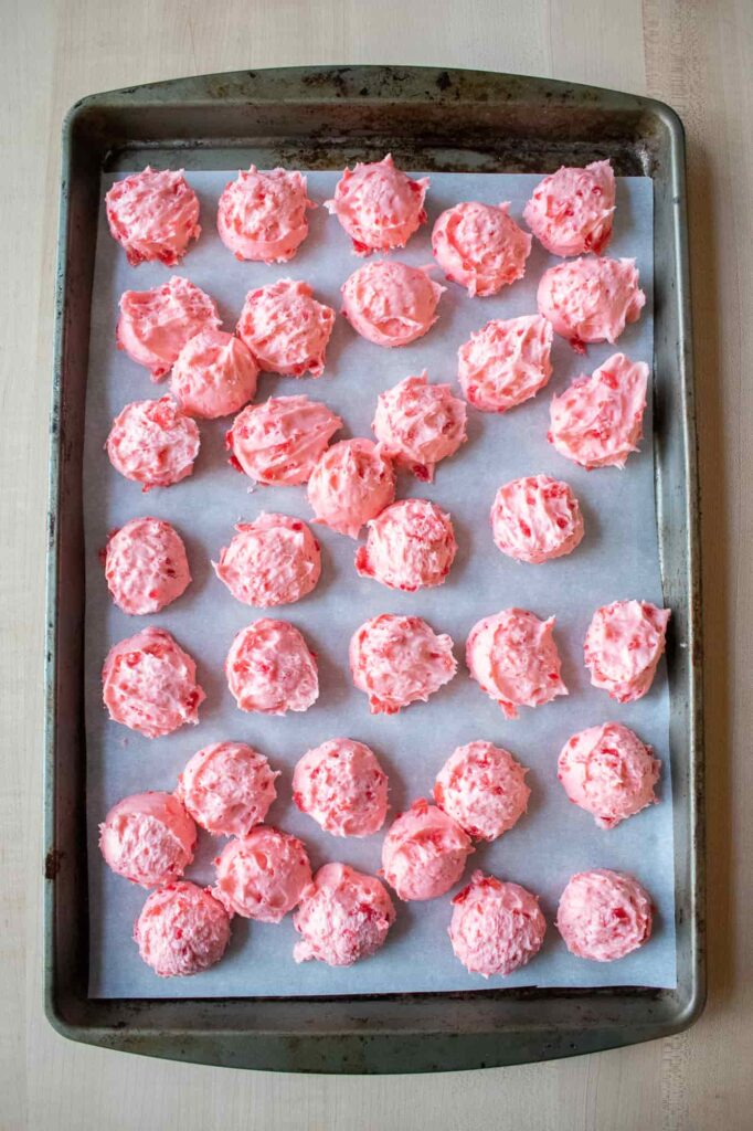 Scoops of pink cherry mash filling scooped onto a parchment-lined baking sheet and ready to freeze.